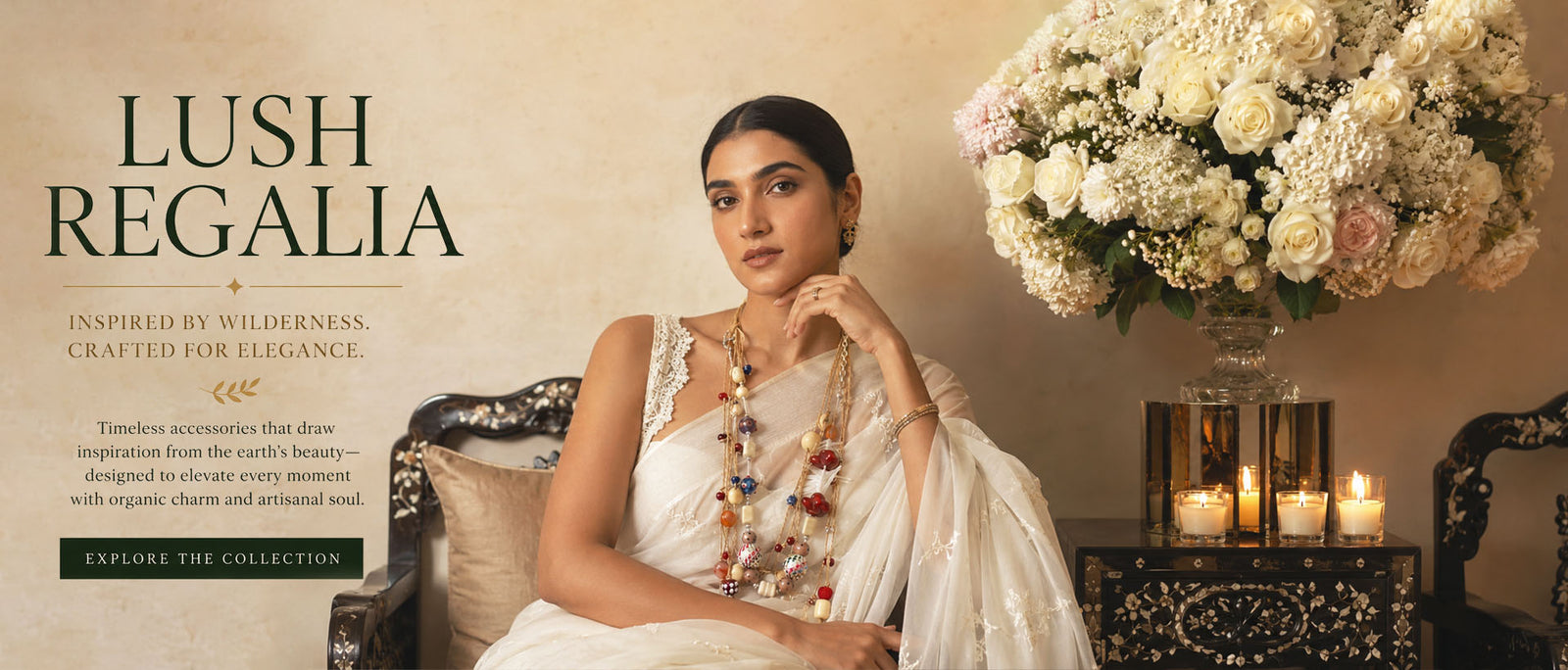 A woman in a white traditional outfit sits in an ornate chair wearing layered statement necklace from coloursutradesigns beside a large floral arrangement and candles, with the collection name 'LUSH REGALIA' 